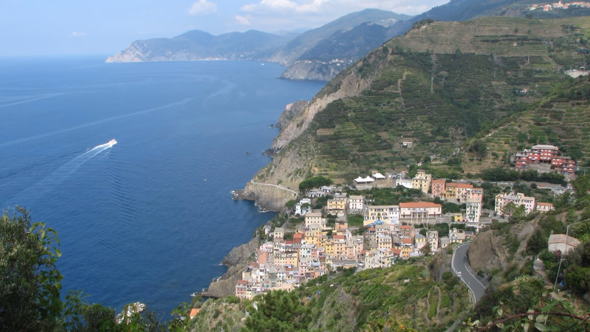 Riomaggiore visto desde la carretera de arriba: el pueblo en la desembocadura de su barranco, los bancales de viña en la ladera y la costa perdiéndose hacia el noroeste.
