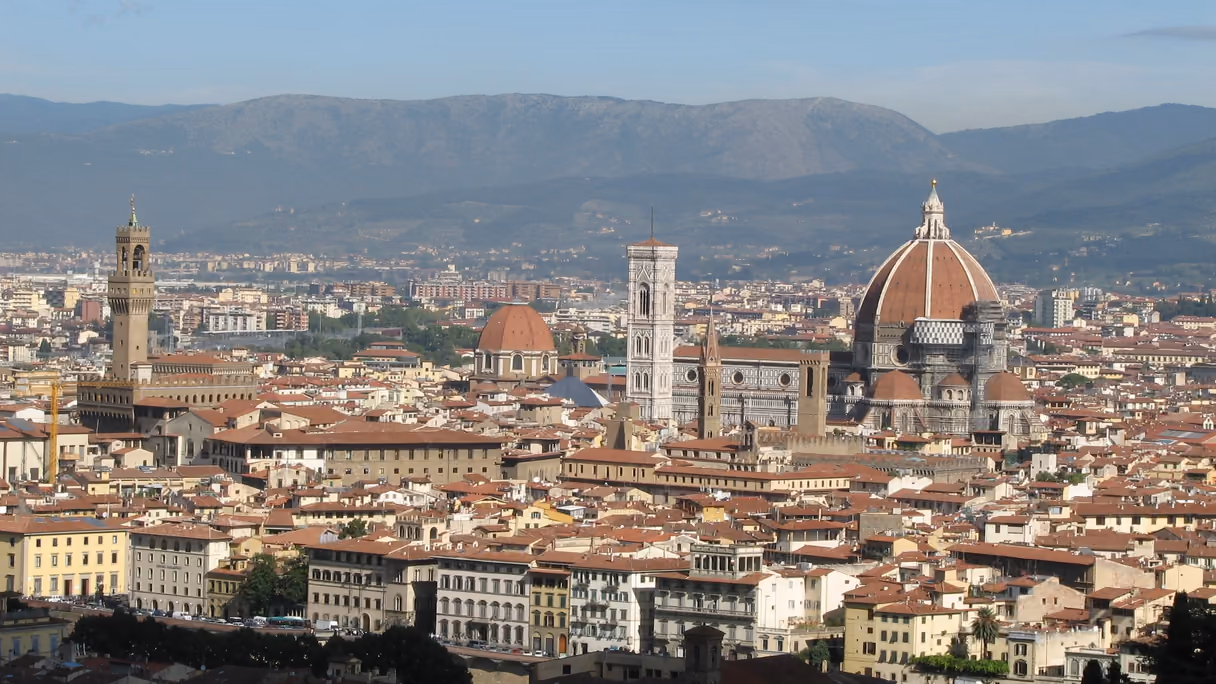 Florencia vista desde el Piazzale Michelangelo a media tarde: un mar de tejados rojos con la cúpula de la catedral y el campanario de Giotto en el centro, la torre del Palazzo Vecchio a la izquierda y los montes al fondo. En el tambor de la cúpula, a la derecha, asoma un andamio.